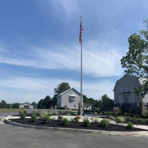 A tall stainless steel tapered flagpole flying a national flag on a landscaped commercial site
