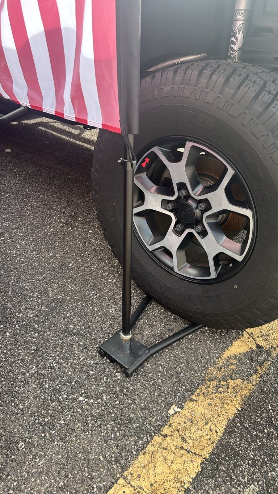 Flag pole base plate with outrigger and caster set at the front wheel of a vehicle